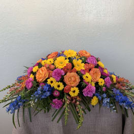 Colorful floral casket spray with orange, yellow, pink, and blue flowers