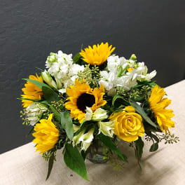 Yellow sunflowers and roses arranged in a glass vase
