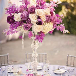 Tall purple and white floral centerpiece on a clear stand
