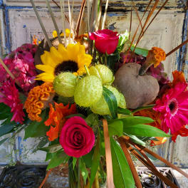 Mixed bouquet with roses, sunflowers, and bright tropical blooms in a glass vase