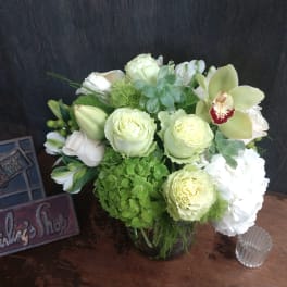 Green and white floral arrangement in a glass vase with orchids and roses