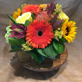 Bright mixed bouquet with gerbera daisies, roses, and sunflowers in a low vase