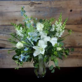 White lilies and roses with blue flowers in a glass vase