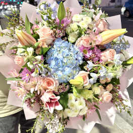 Mixed bouquet with blue hydrangea, pink roses, lilies, and daisies in pink wrap