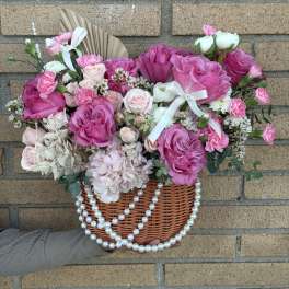 Pink rose bouquet in a wicker basket with white ribbon and pearl strands