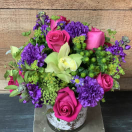 Pink roses and purple flowers arranged in a rustic white vase