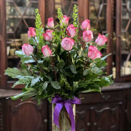 Pink roses in a clear glass vase with a purple ribbon