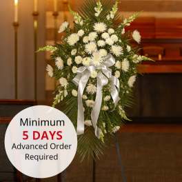 Tall white chrysanthemum standing spray with silver bow on an easel in a chapel setting