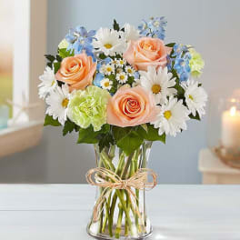 Bouquet of peach roses, white daisies, and blue flowers in a glass vase
