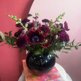 Dark burgundy and purple bouquet in a glossy black vase