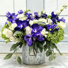 Purple and white floral arrangement in a metal container