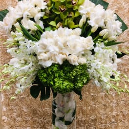 Tall white floral arrangement in a clear glass vase with green orchids