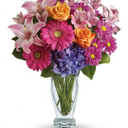 Mixed bouquet of lilies, roses, gerbera daisies, hydrangea, and daisies in a glass vase