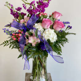 Pink roses and white hydrangeas in a glass vase with purple ribbon