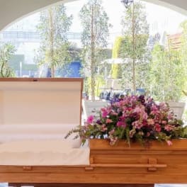 Floral casket spray with pink, purple, and white flowers beside an open casket