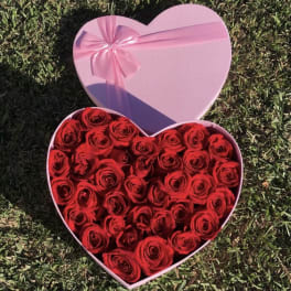 Heart-shaped pink box filled with red roses and a pink ribbon bow