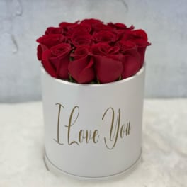 Round white hatbox filled with red roses and gold script reading I Love You.