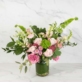 Arrangement of pink roses and mixed blooms with green hydrangea in a clear glass vase