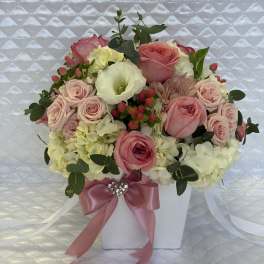 Pink roses and white hydrangeas arranged in a white box with a pink ribbon