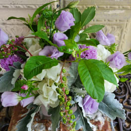 Lavender and white floral arrangement with greenery in a container