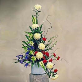 Tall asymmetrical arrangement of white chrysanthemums, red carnations and blue iris in a white vase
