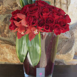 Red roses and coral orchids arranged in a glass vase