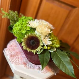 Mixed bouquet with a sunflower, cream roses, and white blooms in a burgundy container