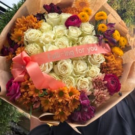 Bouquet of cream roses with orange and purple flowers, wrapped with a pink ribbon