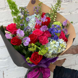 Bouquet of red roses, blue hydrangeas, and purple flowers wrapped in brown paper