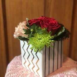 Small floral arrangement in a white geometric box with red, pink, and green blooms