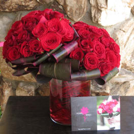 Red rose bouquet in a red glass vase with dark ribbon wrapping