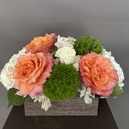 Orange roses and white flowers arranged in a rectangular box with green moss accents