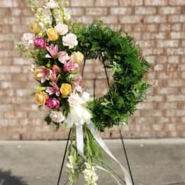 Floral wreath on a stand with pink, yellow, and white blooms