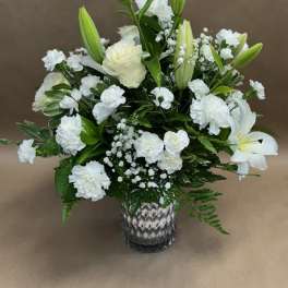 White floral arrangement with lilies, roses, and carnations in a patterned vase