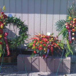 Three standing funeral wreaths with red and orange flowers on easels