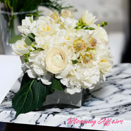 White floral bouquet in a square vase on a marble surface