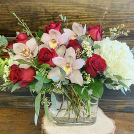 Bouquet of red roses, pale orchids, and white hydrangea in a glass vase