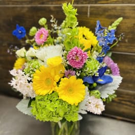 Colorful mixed bouquet in a clear glass vase with yellow, blue, pink, and white blooms