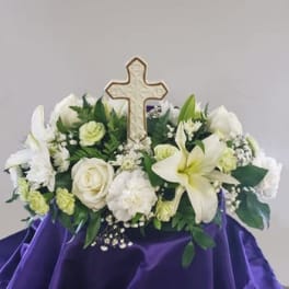 White floral arrangement with a cross centerpiece on purple cloth