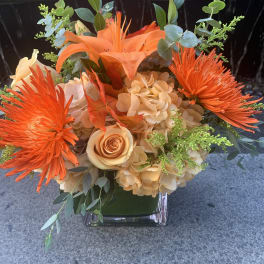 Orange and peach floral arrangement in a clear square vase