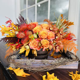 Autumn floral arrangement with orange roses and orchids in a low container