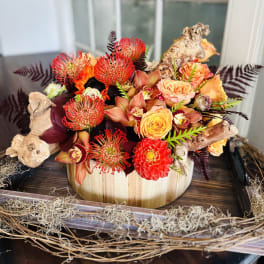 Orange and red floral arrangement in a wooden container with driftwood accents
