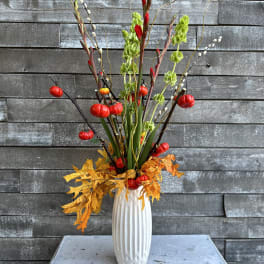 Tall autumn arrangement in a white vase with red and green accents
