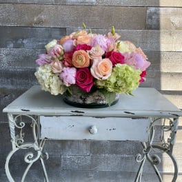 Mixed bouquet of pink, peach, and green flowers in a low container