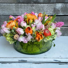 Mixed pink, orange, and lavender flowers in a low glass bowl