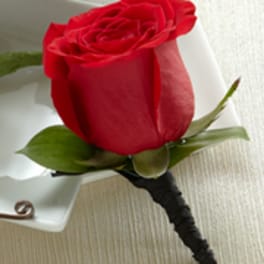 Single red rose boutonniere with black wrapped stem on a white surface
