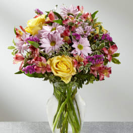 Mixed bouquet of yellow roses, pink daisies, and alstroemeria in a glass vase