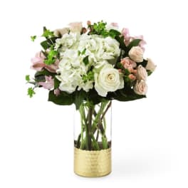 White and blush flowers arranged in a tall glass vase with a gold base
