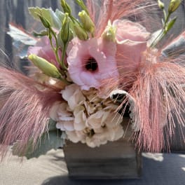 Pink and white floral arrangement with feathery pink accents in a wooden container