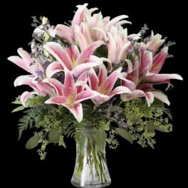 Pink lilies in a clear glass vase with purple filler flowers